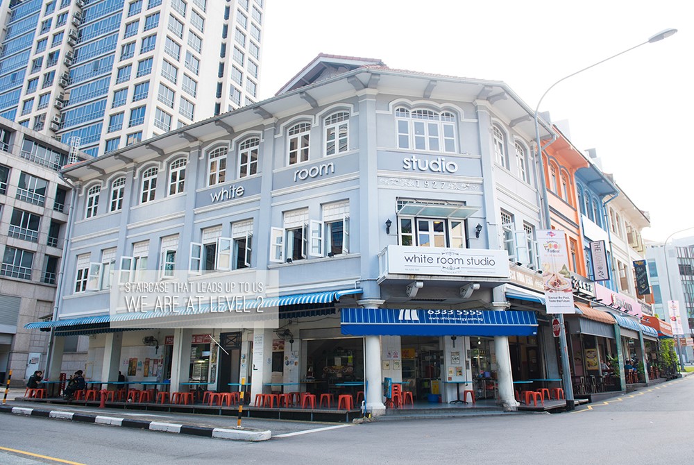 Exterior view of White Room Studio, a light blue building with white trim, in an urban area with high-rise buildings. White Room Studio Singapore