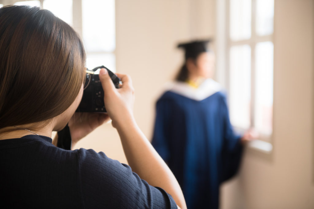 Behind the scenes photo of a photographer taking portraits of a graduate in graduation gown and hat