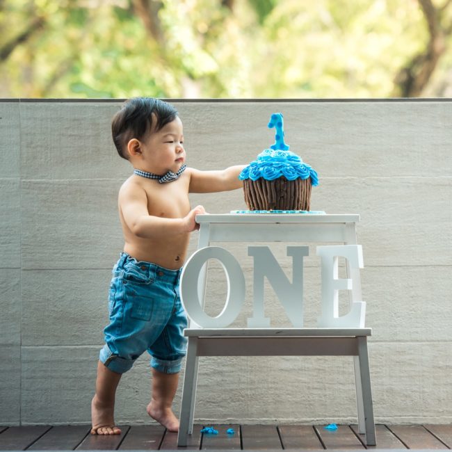 Baby Cake Smash Photography Singapore one year old toddler young boy in bow tie and denim touching giant blue cupcake