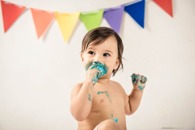 Baby Cake Smash Photography Singapore toddler young boy eating blue cake cream with rainbow party decorations behind him