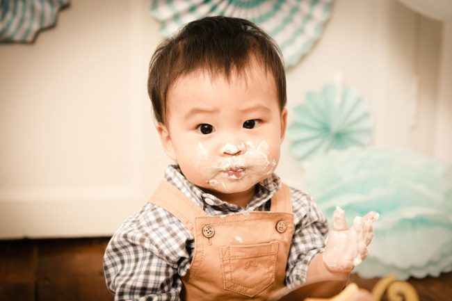 Baby Cake Smash Photography Singapore toddler young boy in brown overalls with cake cream on face and hand