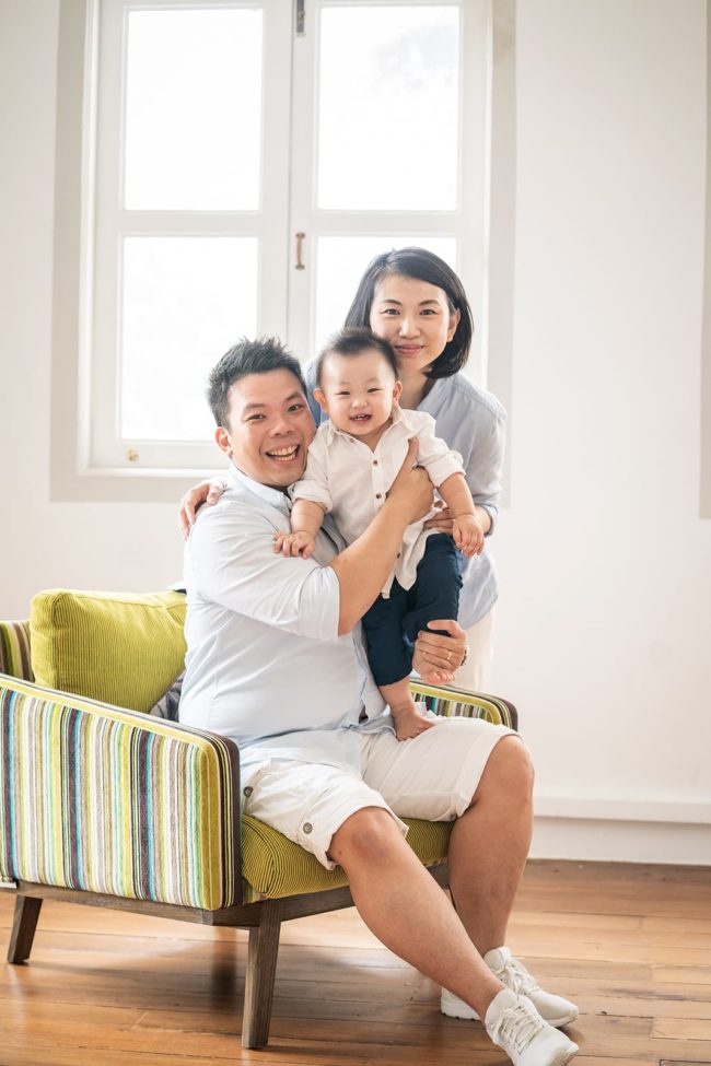 Baby First Year Photography Singapore happy family celebration portrait father sitting on arm chair holding toddler child and mother standing posing for photos