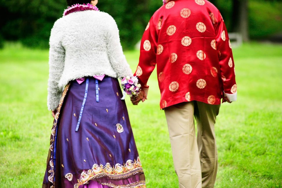 Bridal Photography Singapore bride and groom in traditional indian clothing holding hands and walking in grassy field outdoor photoshoot