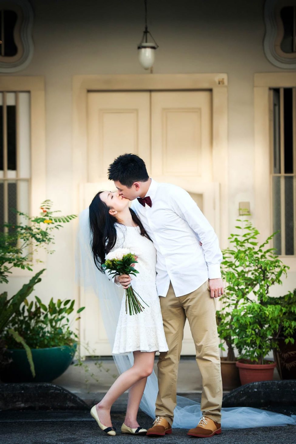 Bridal Photoshoot Singapore bride and groom kissing outside shop house with plants and flower bouquet