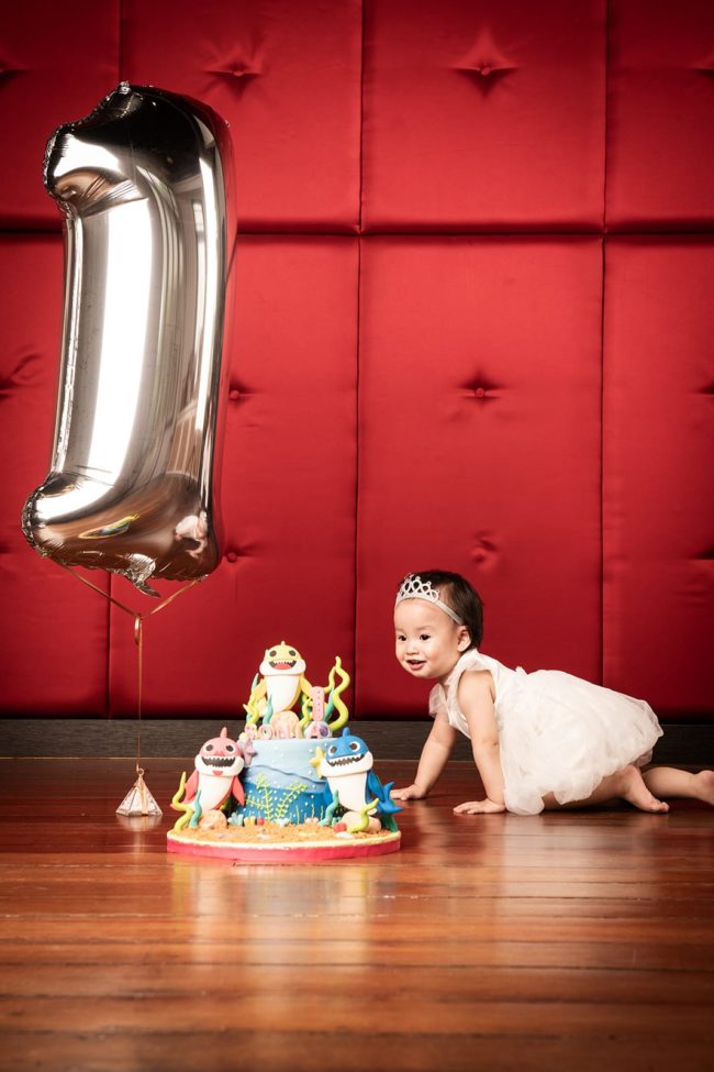Cake Smash Photography Singapore toddler young girl crawling towards baby shark birthday cake with large number 1 balloon