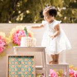 Cake Smash Photography Singapore toddler young girl standing on stool to touch birthday cake with large number 1