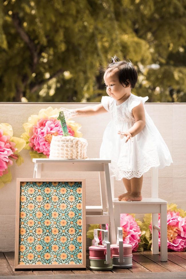 Cake Smash Photography Singapore toddler young girl standing on stool to touch birthday cake with large number 1