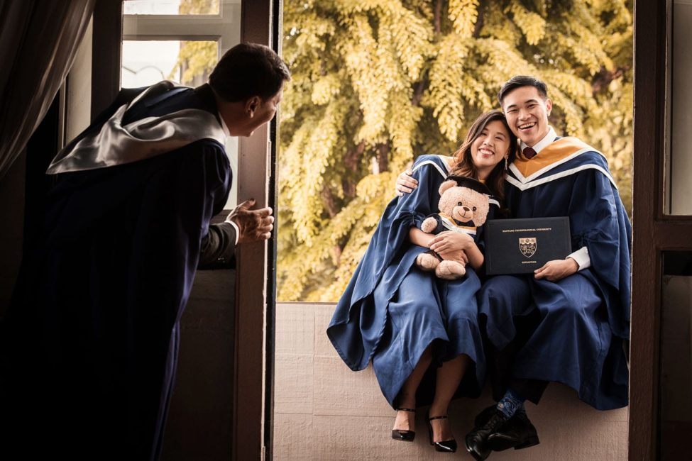 Convocation Photoshoot Package Singapore graduate couple sitting on ledge with teddy bear toy and graduate degree with father looking on by door frame
