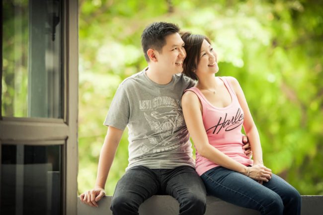 Couple Photoshoot Singapore couple sitting down on ledge with nature landscape background with woman leaning on man