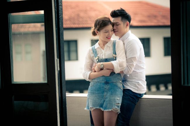 Couple Photoshoot Singapore man leaning on ledge and hugging woman from the back natural light photography