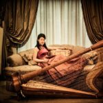 Glamour Photography Singapore woman in modern cheongsam sitting on sofa posing with harp instrument and baroque designed room