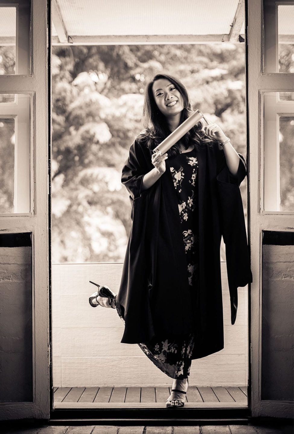 Graduation Photoshoot Package Singapore female graduate holding degree scroll in doorway black and white portrait