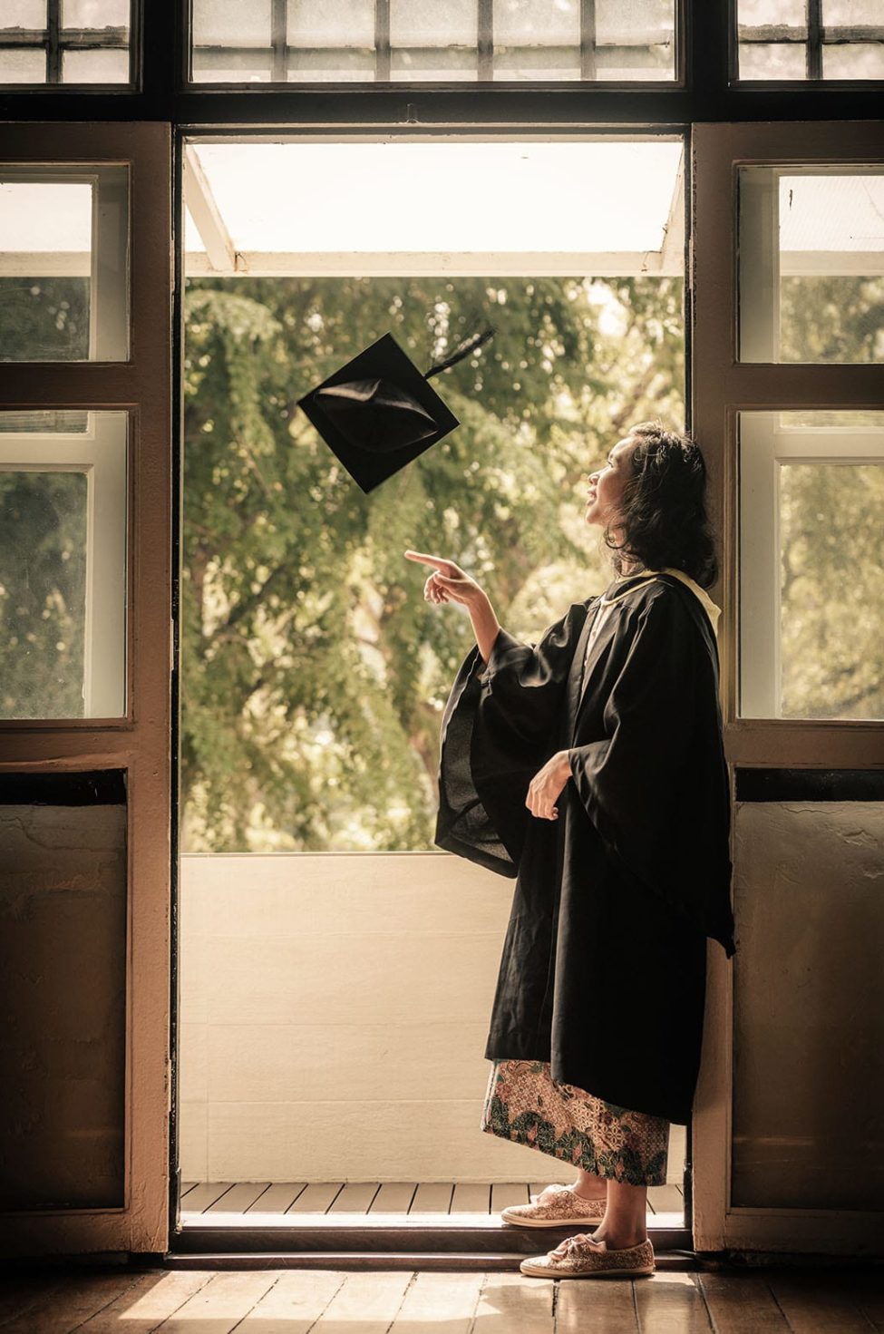 Graduation Photoshoot Singapore graduate leaning against door frame throwing and spinning mortar board
