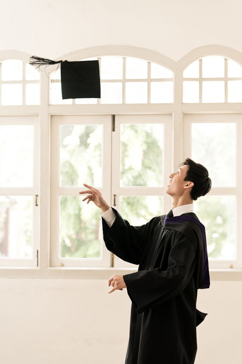 Graduation Portraits Singapore male graduate throwing mortar board candid picture during indoor photoshoot