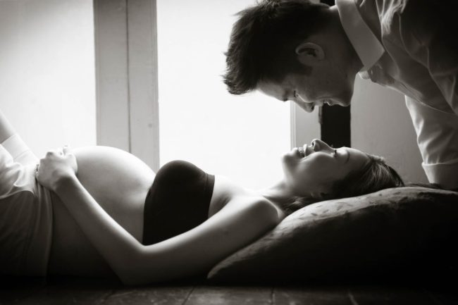 Maternity Photography Singapore boudoir pregnant wife resting on pillow and floor looking at smiling husband black and white portrait photography