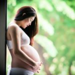 Maternity Photography Singapore pregnant mother holding and looking down at belly with nature landscape background
