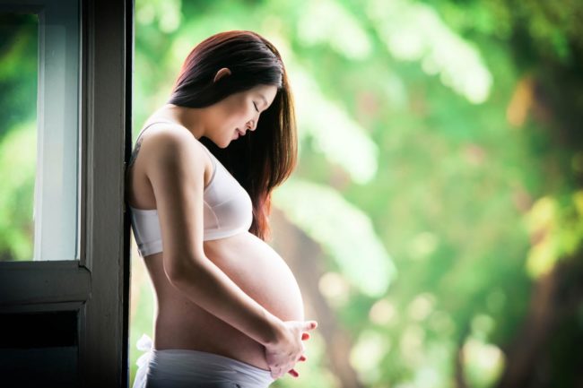 Maternity Photography Singapore pregnant mother holding and looking down at belly with nature landscape background