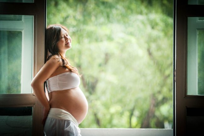 Maternity Photography Singapore pregnant mother in white cloths leaning on door frame with trees in the background