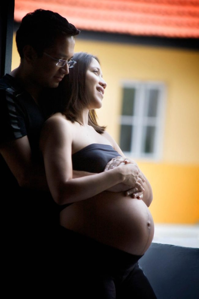 Maternity Photography Singapore pregnant wife leaning on husband standing natural light at door frame