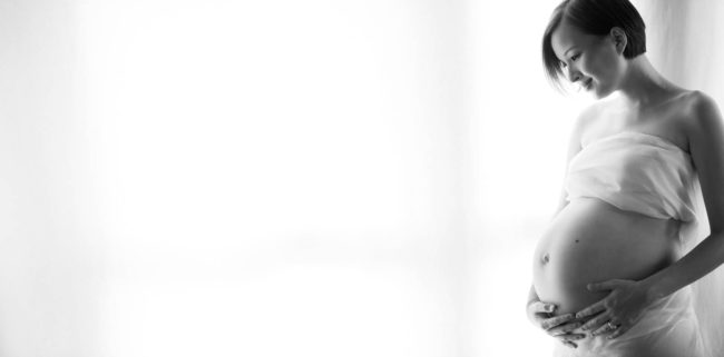 Maternity Photography Singapore pregnant woman in white cloths holding belly and looking down black and white portrait photography