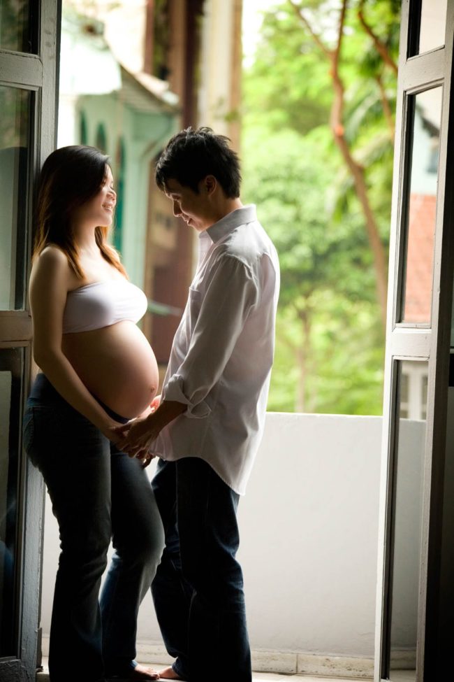 Maternity Photoshoot Singapore casual portrait pregnant wife and husband holding hands at door frame natural light photography