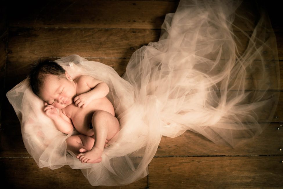 Newborn Photography Singapore baby curled up on white mesh cloths in basket and wooden floor