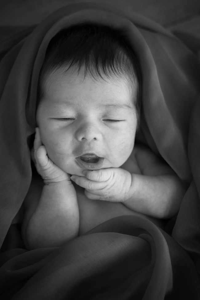 Newborn Photography Singapore baby wrapped up and smiling with hands portrait black and white photography