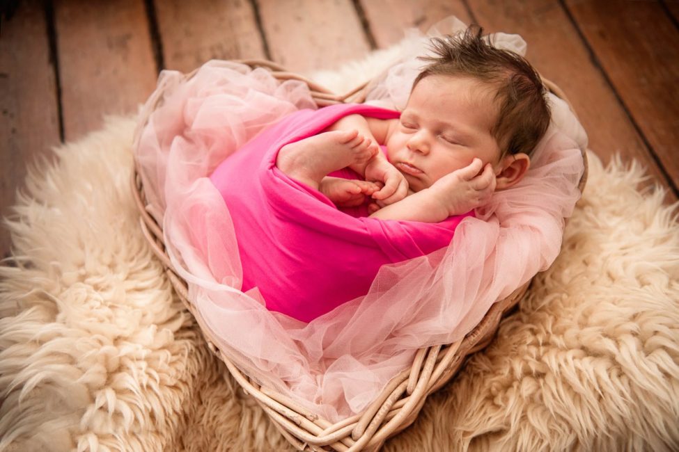 Newborn Photography Singapore baby wrapped up in pink cloths in heart shaped basket over white fur rug