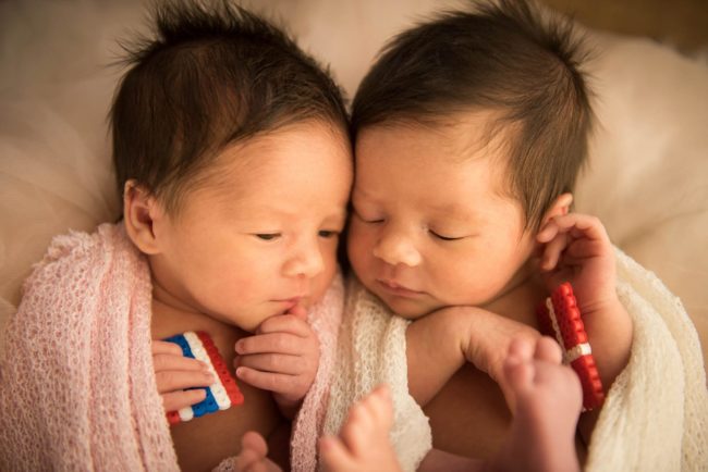 Newborn Photoshoot Singapore 2 babies leaning on each other holding miniature flags and wrapped in soft cloths
