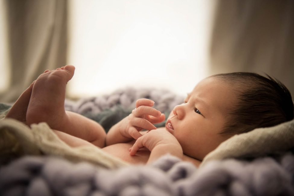 Newborn Photoshoot Singapore baby eyes opened and curled up in grey knit cloths