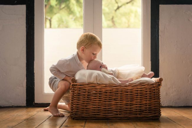 Newborn Photoshoot Singapore brother kissing baby's head baby in basket natural light photography