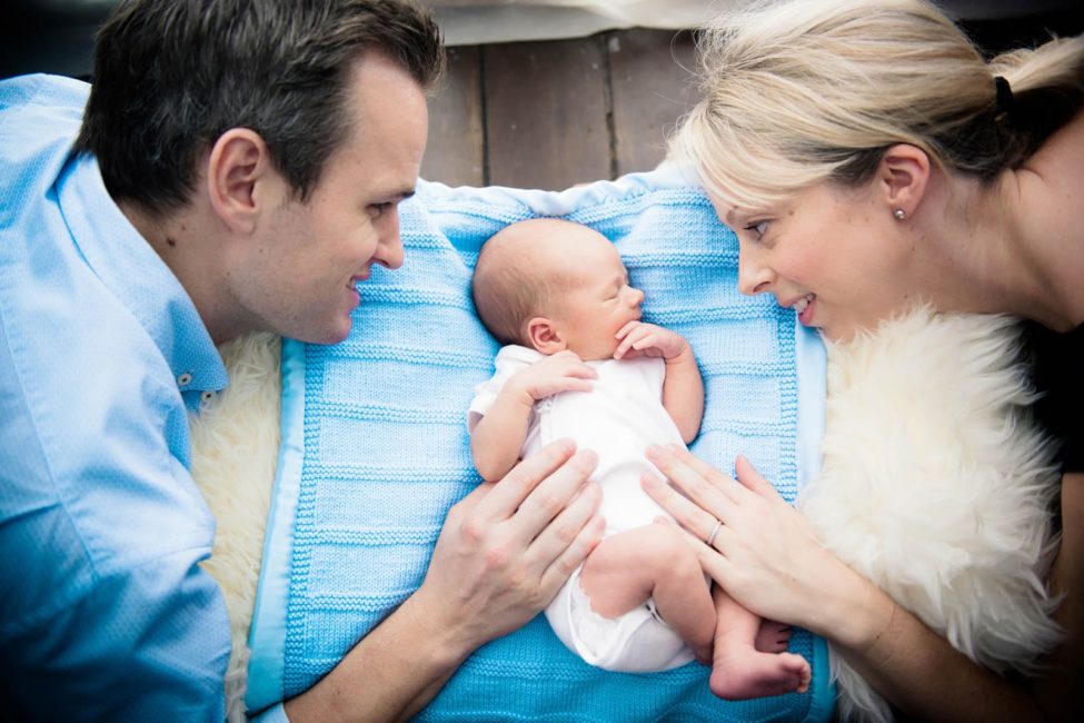 Newborn Photoshoot Singapore father and mother parents looking at and patting sleeping baby on blue cloth and white fur cushion
