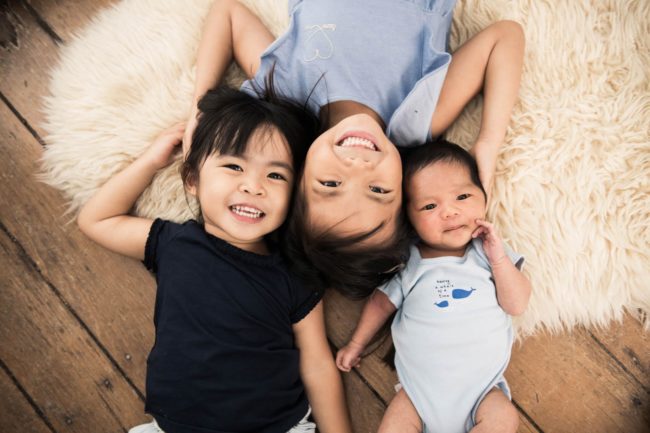 Newborn Photoshoot Singapore siblings and baby family portrait lying on white fur rug and wooden floors