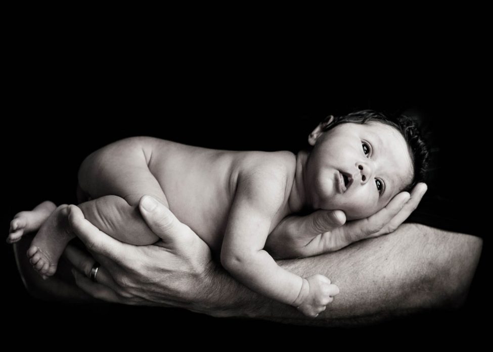 Newborn Shoot Singapore baby cradled in parents arms with eyes open portrait black and white photography