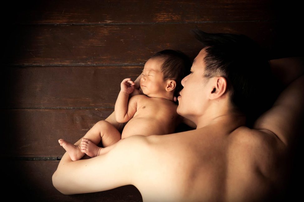 Newborn Shoot Singapore father cradling and facing sleeping baby on wooden floors