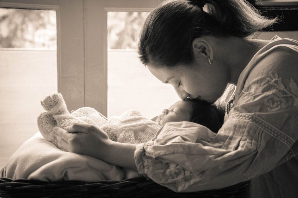 Newborn Shoot Singapore mother cradling baby and kissing baby's forehead black and white portrait photography