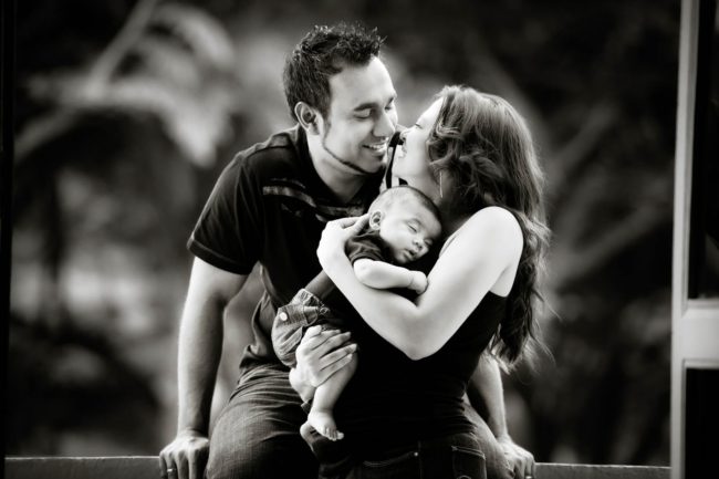 Newborn Shoot Singapore parents smiling at each other and mother carrying sleeping baby black and white portrait photography