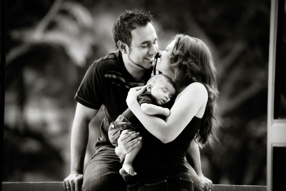 Newborn Shoot Singapore parents smiling at each other and mother carrying sleeping baby black and white portrait photography
