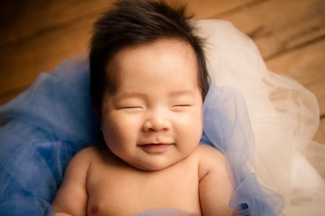 Newborn Shoot Singapore smiling baby with closed eyes lying on blue and white mesh cloths