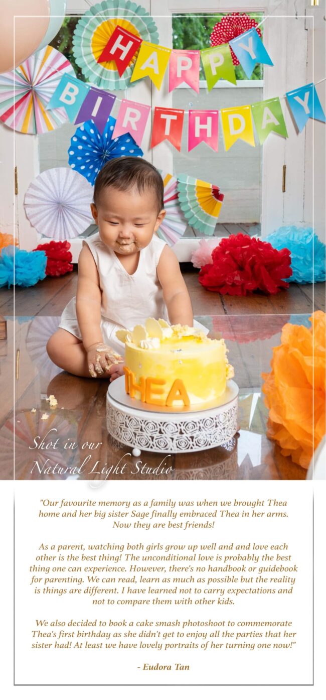 Baby Cake Smash Photography Singapore toddler young girl eating yellow cake cream with rainbow party decorations behind her in a photography studio setting during a first year cake smash photoshoot in Singapore, White Room Studio. Credit: White Room Studio Pte Ltd