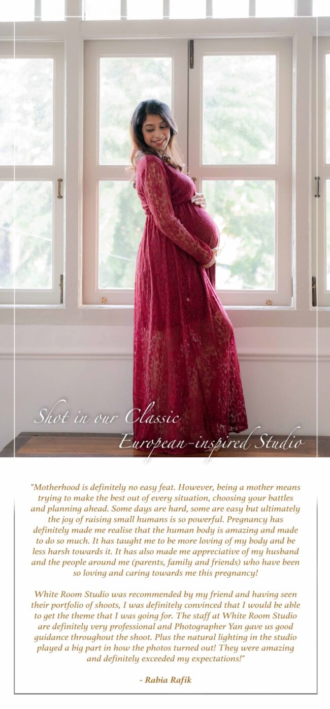 Pregnant mother smiling and standing against tall windows natural light during a professional Maternity photoshoot in Singapore Credit: White Room Studio