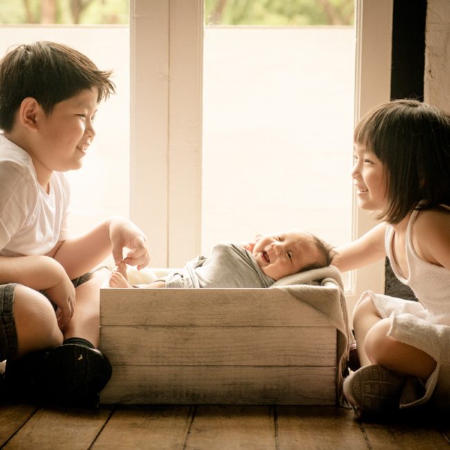 Siblings holding newborn baby at White Room Studio newborn photography session, 219 River Valley Road Singapore. Natural light family and newborn portrait 2026.