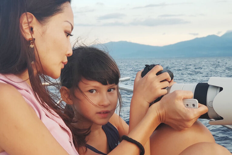 Mother teaching young daughter how to take a photograph by the sea