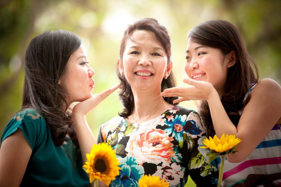 Generation photoshoot session with 2 daughters blowing kisses to their mother holding sunflowers and smiling
