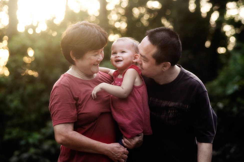 Generation photoshoot outdoors with smiling grandparents carrying young toddler grandchild