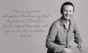 Black and white photo of a smiling man in casual shirt, sitting with a quote on the wall, studio: White Room Studio. White Room Studio Singapore