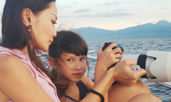 Mother teaching young daughter how to take a photograph by the sea
