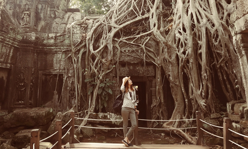 Woman posing at temple ruins with long tree roots