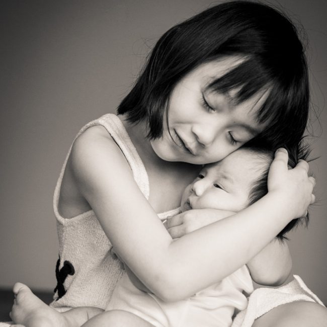Family kids photography session sister hugging her baby brother, photographed by White Room Studio, 219 River Valley Road, Singapore. Natural light family portrait 2026