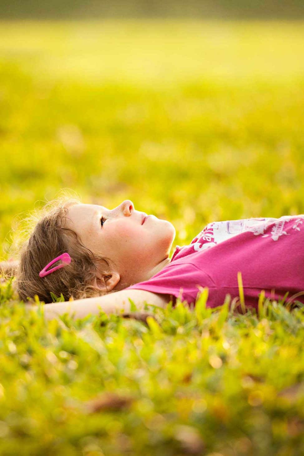 Child Photoshoot Singapore young girl in pink tshirt and hair clip lying on grass
